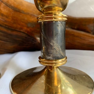 Op de afbeelding: Een paar gouden kandelaars met een zwarte marmeren basis. De kandelaars hebben een ronde basis en een cilindrisch lichaam met een gouden band rond de bovenkant.