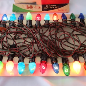 May include: A vintage Holly-lite 25 light multiple set of Christmas lights. The lights are in various colors, including blue, green, red, and yellow. The wires are red and green. The box is visible in the background.