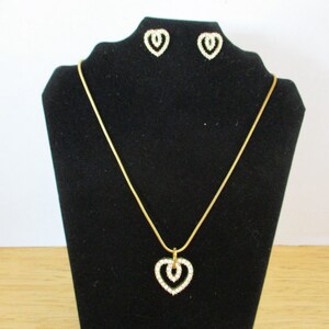 Puede incluir: Un collar de cadena dorada con un colgante de coraz&oacute;n doble y pendientes a juego. Los corazones est&aacute;n engastados con diamantes de imitaci&oacute;n transparentes.