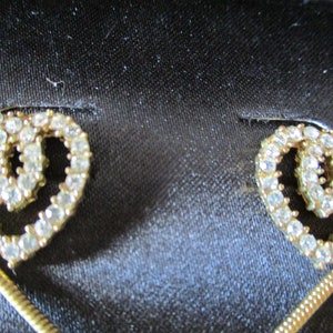 Puede incluir: Un par de pendientes de tono dorado con un dise&ntilde;o de doble coraz&oacute;n, cada coraz&oacute;n est&aacute; incrustado con diamantes de imitaci&oacute;n transparentes.