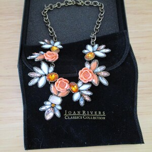 May include: A coral and white statement necklace with a floral design. The necklace is in a black velvet pouch with the text "JOAN RIVERS CLASSICS COLLECTION".