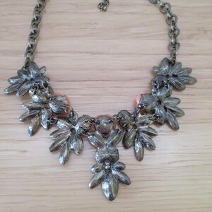 May include: A silver tone statement necklace with a floral design and peach colored accents.