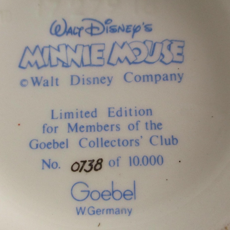 May include: A close-up of a white ceramic item with blue text. The text reads "Walt Disney's Minnie Mouse" and "Limited Edition for Members of the Goebel Collectors' Club." The number "0738 of 10.000" is also visible.
