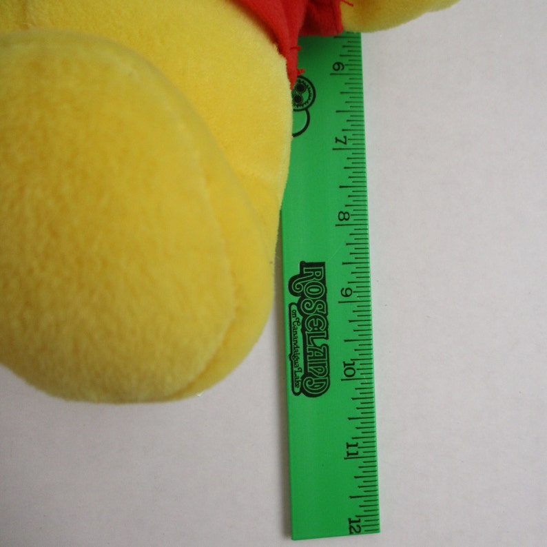 May include: Yellow plush Winnie the Pooh bear with a red shirt. The bear is approximately 10 inches tall.