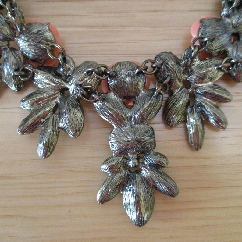 May include: A silver tone necklace with a floral design. The necklace features several flower-shaped pendants with a pink center. The necklace is made of metal and has a chain link design.