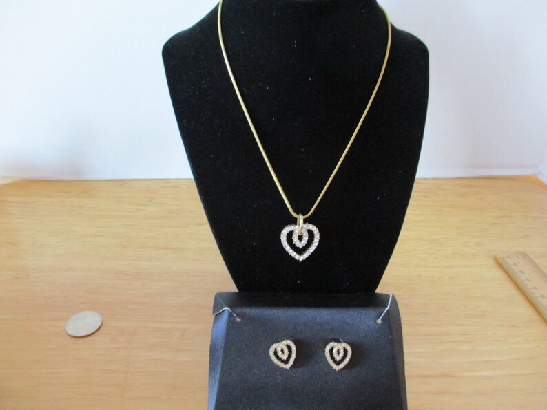 Puede incluir: Un collar de oro con un colgante de doble coraz&oacute;n engastado con diamantes de imitaci&oacute;n transparentes. Pendientes a juego con dise&ntilde;o de doble coraz&oacute;n y diamantes de imitaci&oacute;n transparentes.