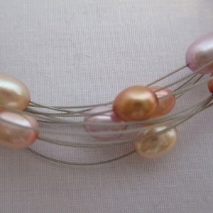 Op de afbeelding: Een meerstrengs ketting met een zilveren draad en roze, perzikkleurige en lavendelkleurige parels.