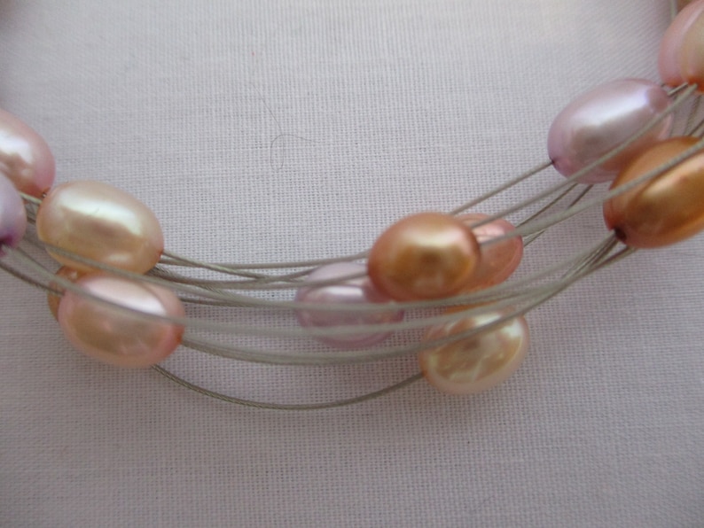 Op de afbeelding: Een meerstrengs ketting met een zilveren draad en roze, perzikkleurige en lavendelkleurige parels.