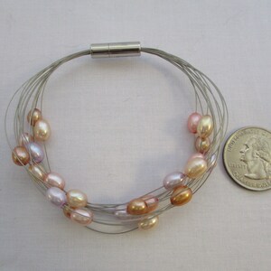 Op de afbeelding: Een zilveren draad armband met een magnetische sluiting en meerdere strengen parels in tinten roze, perzik en lavendel.