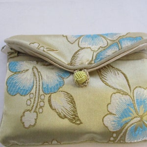 Op de afbeelding: Een kleine, gouden clutch met een bloemenpatroon. De clutch heeft een blauw en wit bloemenpatroon met een gele knoopsluiting.