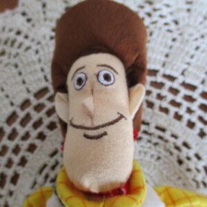 Puede incluir: Un peluche de un personaje de dibujos animados con cara color beige, pelo casta&ntilde;o y sombrero de vaquero. El personaje tiene una expresi&oacute;n sonriente y lleva una camisa amarilla con detalles rojos. Juguete coleccionable para ni&ntilde;os.