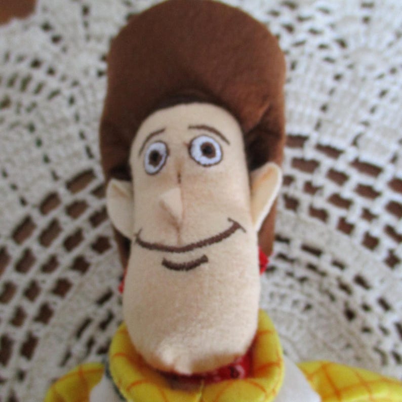 Puede incluir: Un peluche de un personaje de dibujos animados con cara color beige, pelo casta&ntilde;o y sombrero de vaquero. El personaje tiene una expresi&oacute;n sonriente y lleva una camisa amarilla con detalles rojos. Juguete coleccionable para ni&ntilde;os.