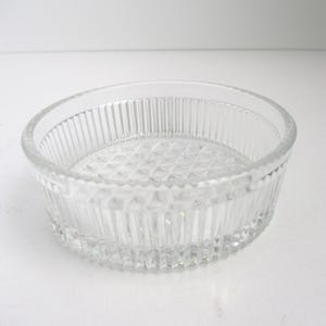 May include: A clear glass bowl featuring a circular shape with vertical ribbed detailing along the exterior walls and a textured diamond pattern embossed on the interior base. The rim is smooth and rounded, providing a clean edge to the vessel.