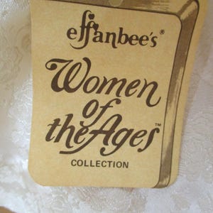 Puede incluir: Una etiqueta de papel marr&oacute;n con el texto "Effanbee's Women of the Ages Collection" en letras marrones.