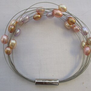 Op de afbeelding: Een zilveren draad armband met een magnetische sluiting heeft meerdere strengen parels in tinten roze, lavendel en cr&egrave;me.