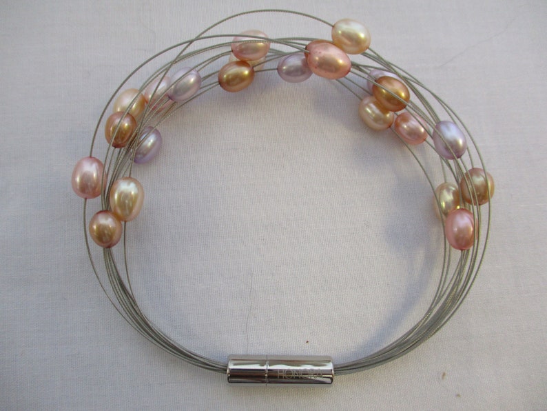 Op de afbeelding: Een zilveren draad armband met een magnetische sluiting heeft meerdere strengen parels in tinten roze, lavendel en cr&egrave;me.