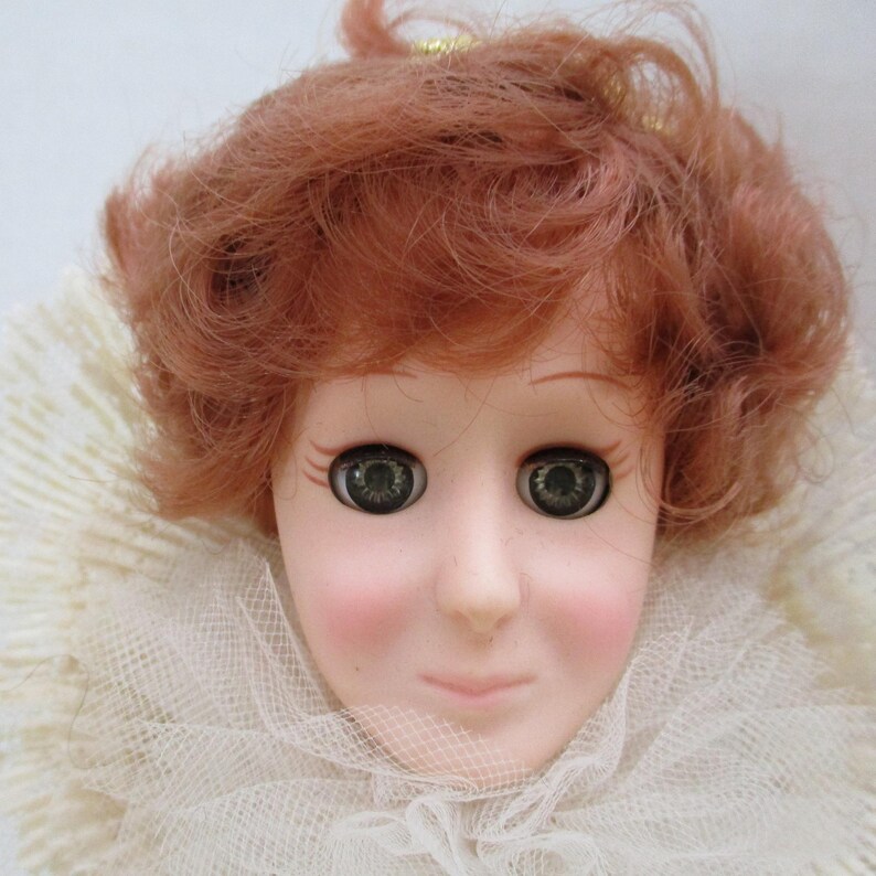 Puede incluir: Una cabeza de mu&ntilde;eca de porcelana con cabello rojo rizado, ojos verdes y un cuello de encaje blanco.