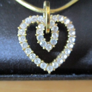 Puede incluir: Un collar de cadena dorada con un colgante de coraz&oacute;n doble. El colgante est&aacute; hecho de diamantes de imitaci&oacute;n transparentes.