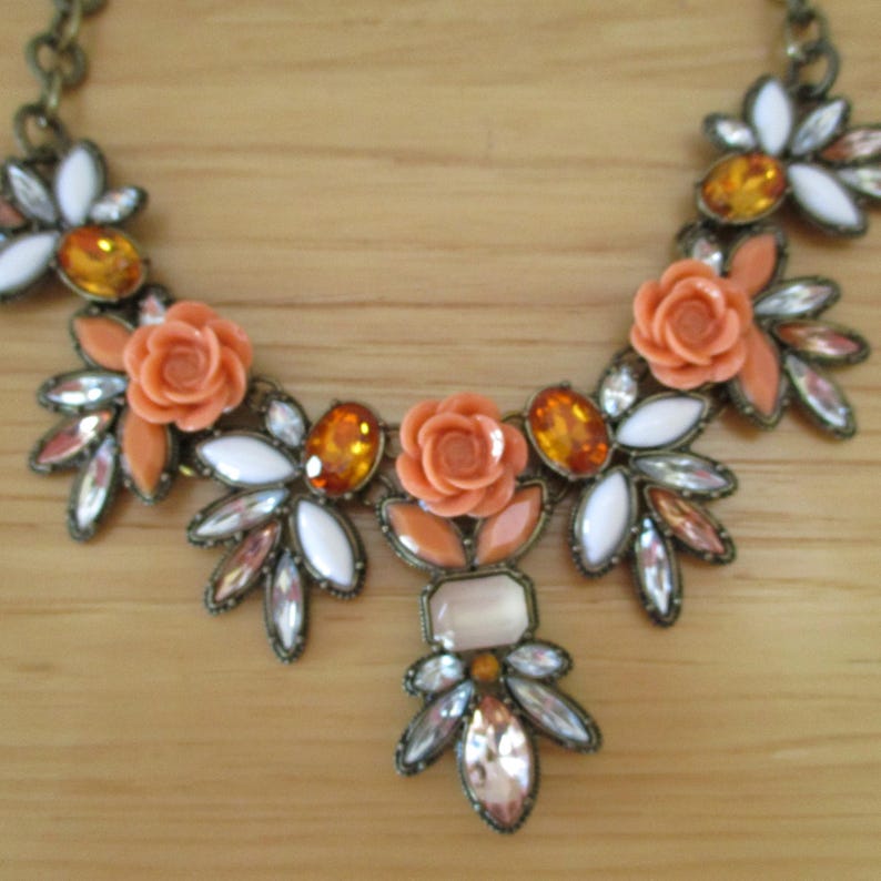 May include: A statement necklace with a floral design featuring orange and white flowers and clear and amber rhinestones.