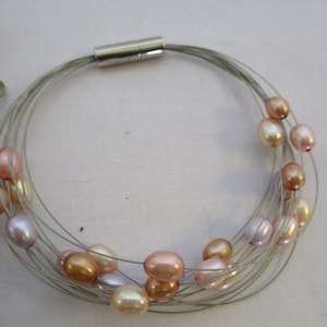 Op de afbeelding: Een zilveren draadketting met een magneetsluiting en meerdere strengen parels in tinten roze, perzik en lavendel.