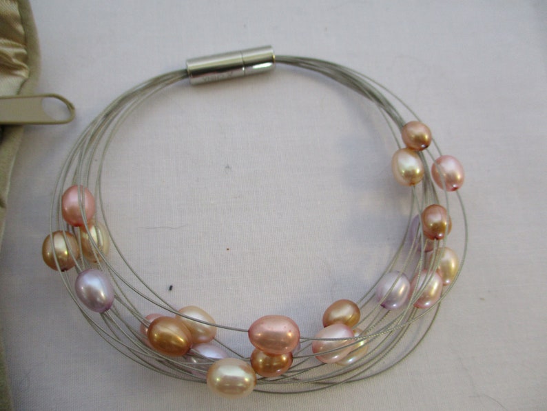 Op de afbeelding: Een zilveren draadketting met een magneetsluiting en meerdere strengen parels in tinten roze, perzik en lavendel.