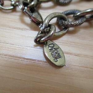 May include: Close-up of a gold-toned chain necklace with a small oval tag that reads "Joan Miro".