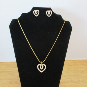Puede incluir: Un collar de cadena dorada con un colgante de coraz&oacute;n doble y pendientes a juego. Los corazones est&aacute;n engastados con diamantes de imitaci&oacute;n transparentes.