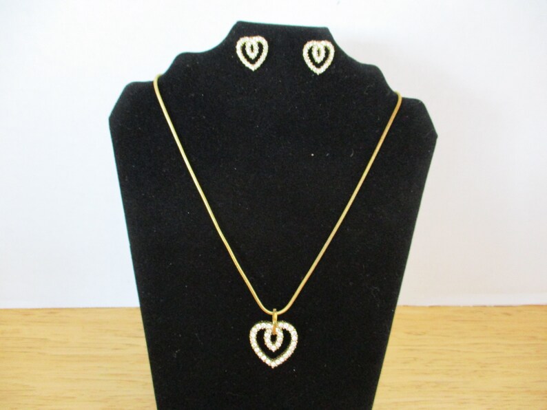 Puede incluir: Un collar de cadena dorada con un colgante de coraz&oacute;n doble y pendientes a juego. Los corazones est&aacute;n engastados con diamantes de imitaci&oacute;n transparentes.
