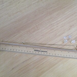 Puede incluir: Un conjunto de collar y pendientes de oro con un colgante en forma de coraz&oacute;n y pendientes a juego. El colgante y los pendientes est&aacute;n adornados con brillantes transparentes.