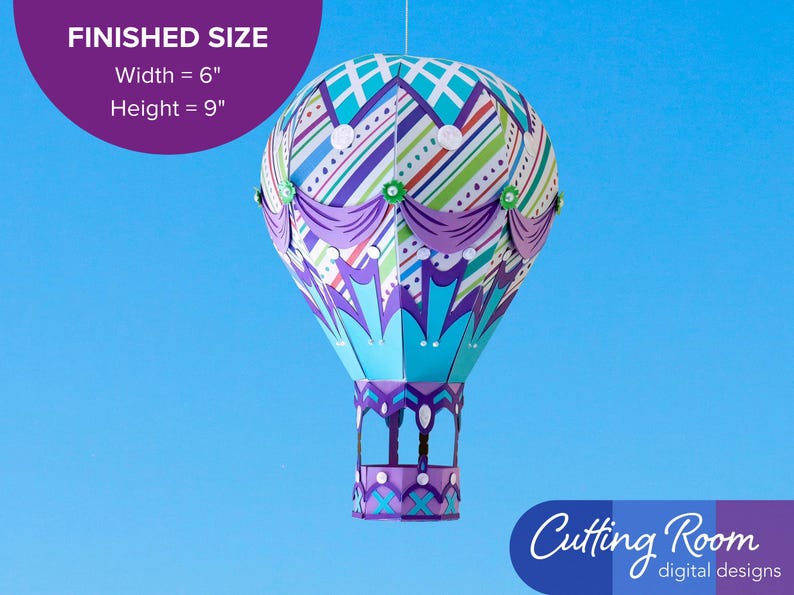 A papercraft hot air balloon with a striped pattern in shades of blue, green, purple, and white. The balloon has purple swag accents and silver embellishments.  A banner indicates that the balloon is about 6 inches wide and 9 inches tall.