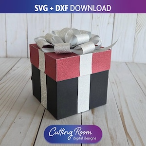 May include: A decorative gift box with a red glitter top and black base, accented with silver glitter stripes and a silver bow. The box has the text "SVG + DXF DOWNLOAD" and "Cutting Room digital designs".