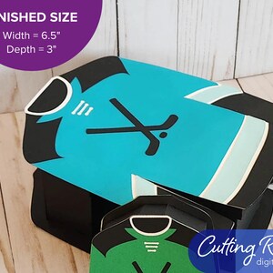 The large gift box shaped like a hockey jersey has crossed hockey sticks and a puck on the front.  There is a banner that says the box is 6.5 inches wide and 3 inches deep.