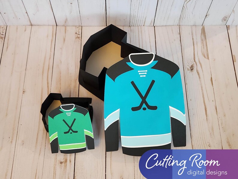 Two hockey jersey shaped boxes, one is green and the other is blue. Both boxes have a hockey stick design and are open to reveal the inside. The text 'Cutting Room digital designs' is at the bottom of the image.