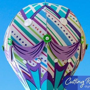 A papercraft hot air balloon with a striped pattern in shades of blue, green, purple, and white. The balloon has a purple trim and green accents. The text 'Cutting Room digital designs' is visible in the lower right corner of the image.