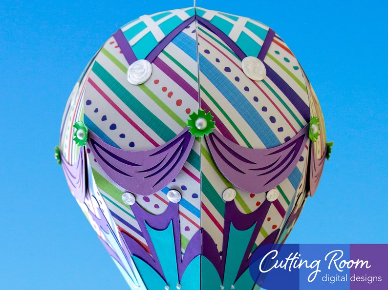 A papercraft hot air balloon with a striped pattern in shades of blue, green, purple, and white. The balloon has a purple trim and green accents. The text 'Cutting Room digital designs' is visible in the lower right corner of the image.