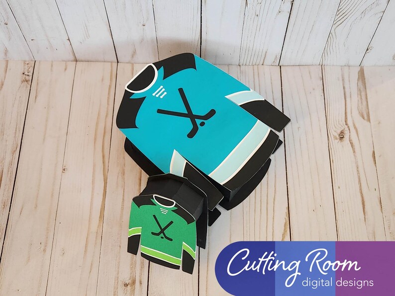 May include: Two hockey jersey shaped boxes, one blue and one green, with a hockey stick and puck graphic. The boxes are layered on top of each other. The text "Cutting Room digital designs" is visible in the bottom right corner.