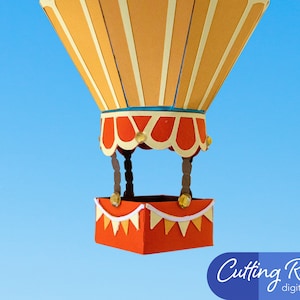 A papercraft hot air balloon with an orange and white striped basket and a yellow and orange striped balloon. The balloon is suspended against a blue sky background. The basket has a white and orange pennant trim.