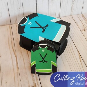 A hockey jersey shaped box with a blue and white jersey design and a smaller gift card or treat box size hockey jersey box is next to it.