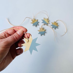 Könnte beinhalten: Fünf goldene und blaue sternförmige Anhänger mit Schnur. Die Sterne sind halb golden und halb blau bemalt.