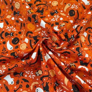Op de afbeelding: Oranje stof met een Halloween-patroon. Het ontwerp bevat zwarte katten, witte geesten, pompoenen, vleermuizen, sterren en andere griezelige elementen. Geschikt voor knutselprojecten en seizoensgebonden decoraties.