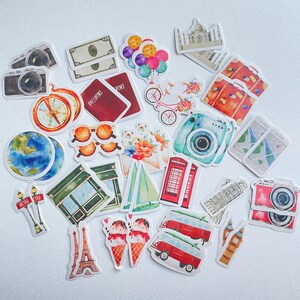 Op de afbeelding: Een verzameling stickers met een reisthema, voorzien van illustraties van camera's, paspoorten, een kompas, een wereldbol, een zonnebril, ballonnen, een fiets, koffers, een smartphone, een rode telefooncel, een zeilboot, de Eiffeltoren, ijsjes en busjes.