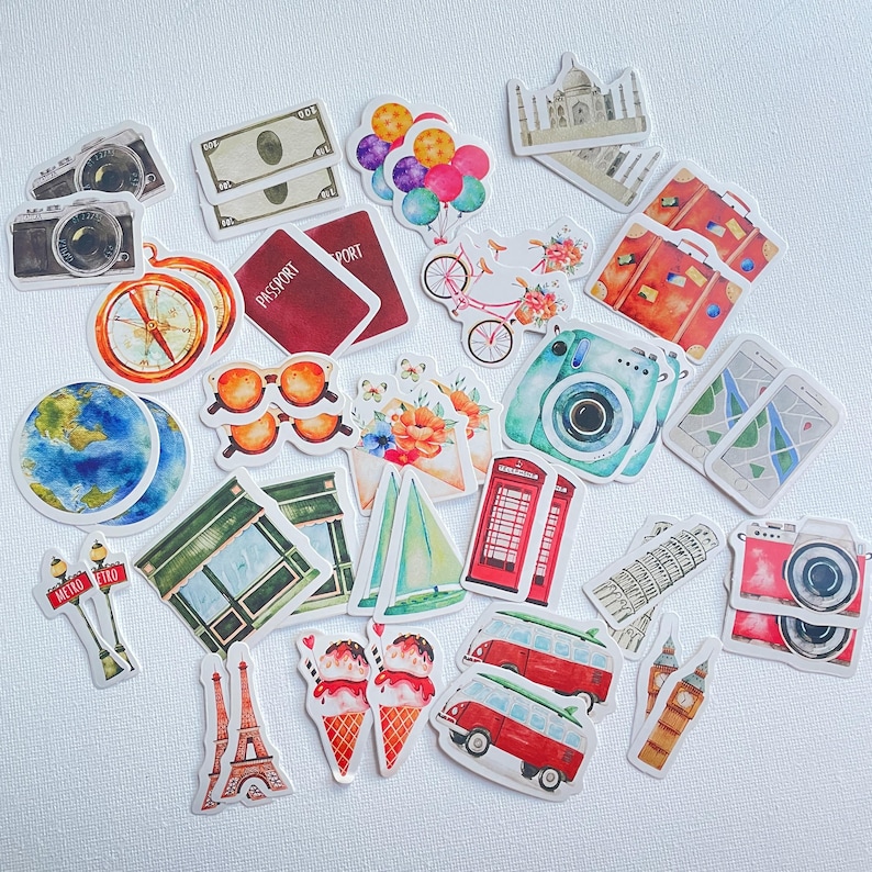Op de afbeelding: Een verzameling stickers met een reisthema, voorzien van illustraties van camera's, paspoorten, een kompas, een wereldbol, een zonnebril, ballonnen, een fiets, koffers, een smartphone, een rode telefooncel, een zeilboot, de Eiffeltoren, ijsjes en busjes.