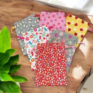 May include: Six small fabric drawstring bags with different patterns. The bags are made of cotton and have a variety of colors, including pink, yellow, red, and gray. The patterns include strawberries, ladybugs, bees, flowers, and birds.