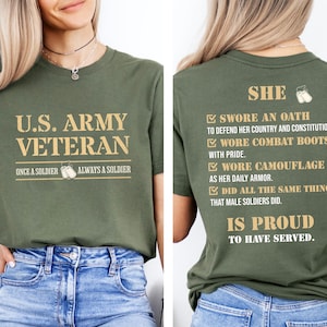 Op de afbeelding: Een groen T-shirt met de tekst "U.S. ARMY VETERAN" op de voorkant en de tekst "SHE SWORE AN OATH TO DEFEND HER COUNTRY AND CONSTITUTION. WORE COMBAT BOOTS WITH PRIDE. WORE CAMOUFLAGE AS HER DAILY ARMOR. DID ALL THE SAME THINGS THAT MALE SOLDIERS DID. IS PROUD TO HAVE SERVED." op de achterkant.