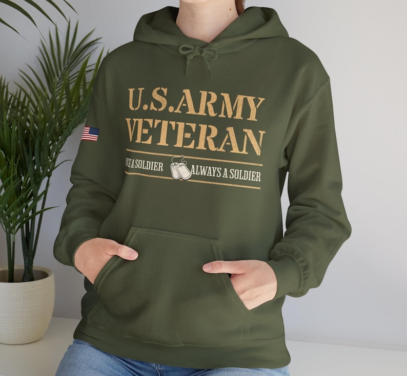 Op de afbeelding: Een groen hoodie met de tekst "U.S. ARMY VETERAN" in gouden letters. De tekst "Once a soldier, always a soldier" staat onder de hoofdtekst. Een kleine Amerikaanse vlag bevindt zich op de linkermouw.