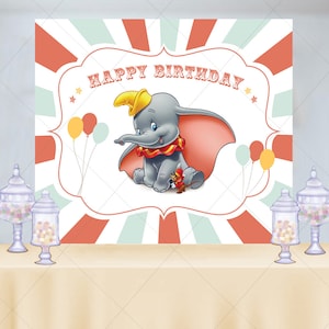 May include: A Dumbo-themed birthday party backdrop featuring the text "HAPPY BIRTHDAY" above an illustration of Dumbo the elephant. The backdrop has a red and white striped design with balloons and is set up with a table and candy jars.