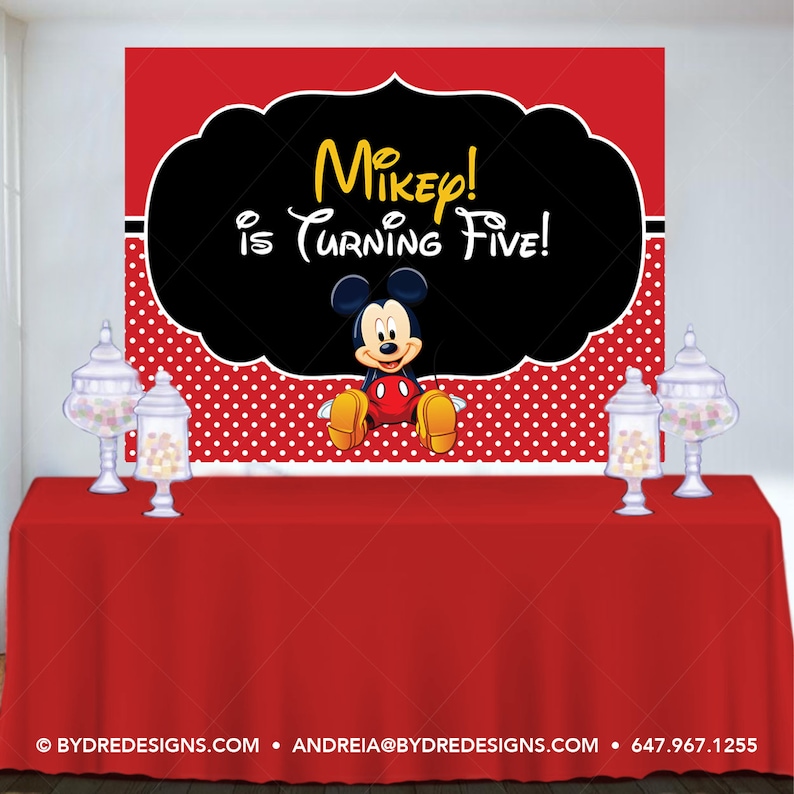 K&ouml;nnte beinhalten: Eine rote Tischdecke mit einem Hintergrund mit Micky Maus und dem Text "Mikey! is Turning Five!". Der Hintergrund hat eine schwarze Form mit gelbem Text, ein rot-wei&szlig;es Tupfenmuster und einen roten oberen Rand. Glasbeh&auml;lter mit S&uuml;&szlig;igkeiten stehen auf dem Tisch.