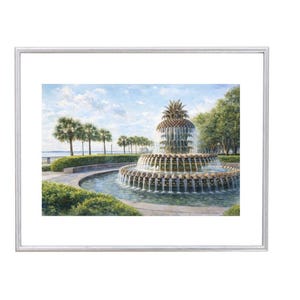 May include: A framed watercolour print depicting a tiered fountain topped with a pineapple. The fountain is set amidst greenery, palm trees, and a blue sky. The artwork is presented in a silver frame.
