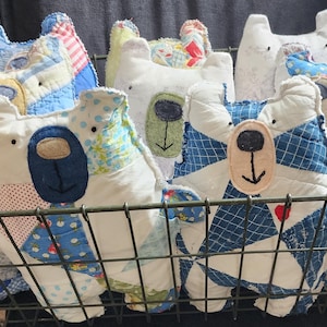 May include: A wire basket filled with handmade patchwork teddy bears. The bears are made from a variety of fabrics, including blue, white, and green. They have embroidered faces and are all different sizes.