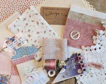 May include: A collection of fabric scraps, lace, buttons, and other sewing supplies in pink, white, and blue tones. The supplies are arranged on a wooden surface. The text "ReDesign 614 remake redesign reuse" is visible on a brown tag. The text "Just for you Have a happy day" is visible on a white tag.
